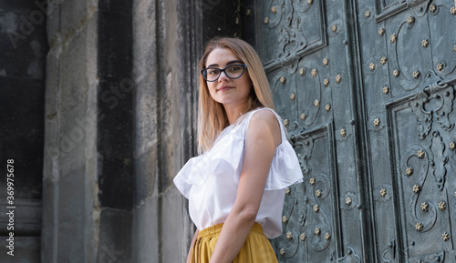 Young elegant girl posing at city street. Pretty beautiful business woman in elegant white sundress and yellow pants