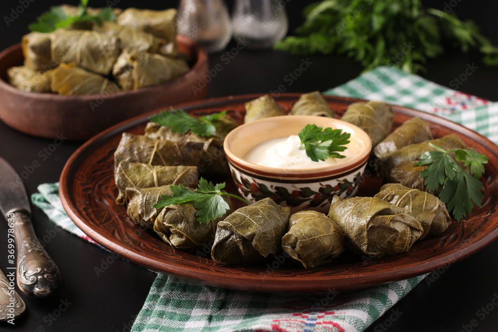 Stuffed grape leaves - traditional Mediterranean cuisine, Dolma on a brown plate with fresh parsley and garlic sauce on a black background, Closeup Stuffed grape leaves - traditional Mediterranean cuisine, Dolma on a brown plate with fresh parsley and garlic sauce on a black background, Closeup