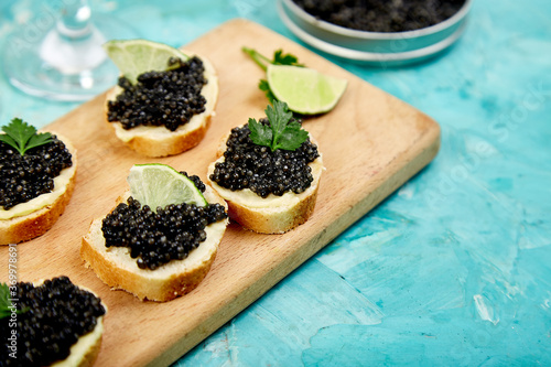 Sturgeon black caviar in wooden bowl, sandwiches and champagne on white background copy space.