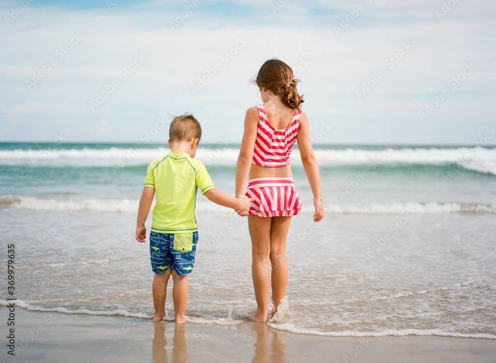 Big sister holding little brother's hand while walking towards the ocean Big sister holding little brother's hand while walking towards the ocean