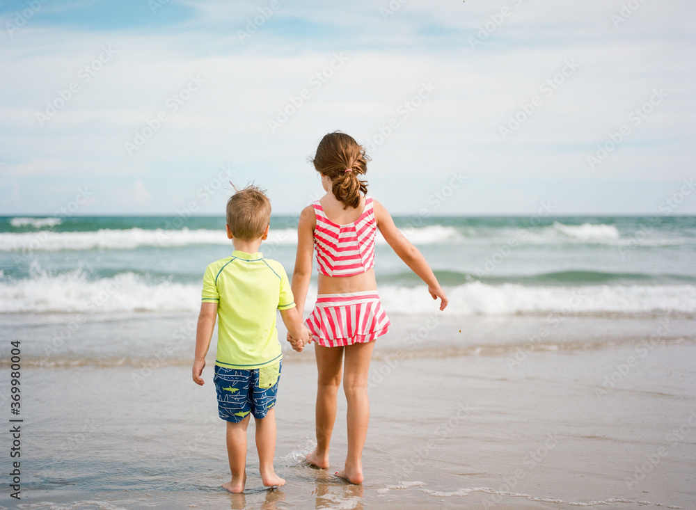 Big sister holding little brother's hand while walking towards the ocean Big sister holding little brother's hand while walking towards the ocean