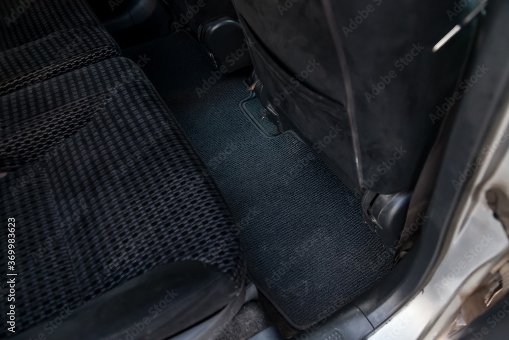 Dirty dark fabric car mats under the rear passenger seat before being dry cleaned at a auto service center. Pre-sale preparation. Dirty dark fabric car mats under the rear passenger seat before being dry cleaned at a auto service center. Pre-sale preparation.
