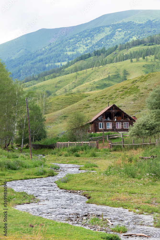 A fast mountain stream and a wooden house on a background of mountains, Altai Siberia