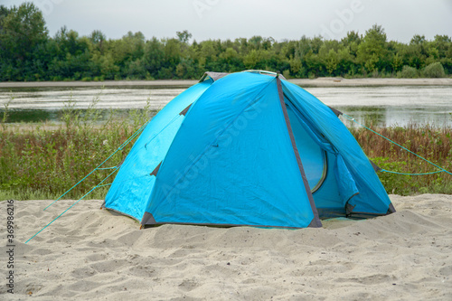 Blue tent on a sandy beach by the river.