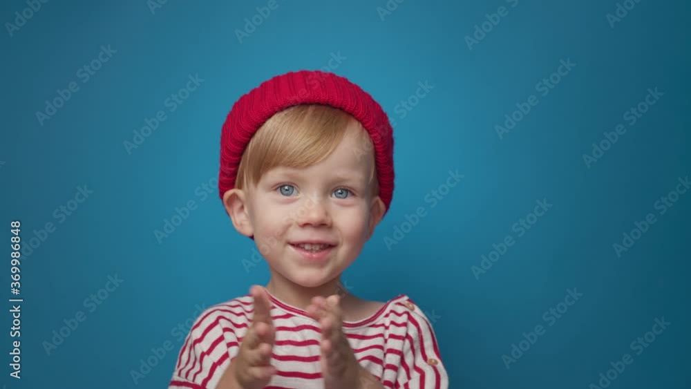 handsome blue-eyed boy in a red hat on a blue background applauds and laughs handsome blue-eyed boy in a red hat on a blue background applauds and laughs