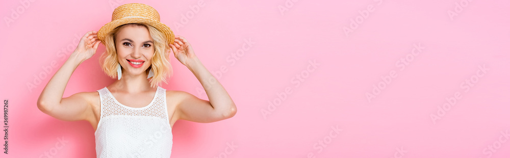 panoramic crop of young woman touching straw hat on pink panoramic crop of young woman touching straw hat on pink