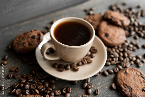 Coffee cup with cookies on wooden table background. Mug of black coffee with scattered coffee beans and cookies on a wooden table. Fresh coffee beans.