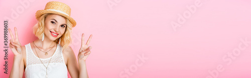 panoramic crop of woman in straw hat showing peace sign on pink