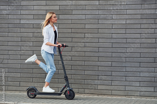 Fotografie Side view of beautiful blonde in casual clothes that riding electric schooter ou