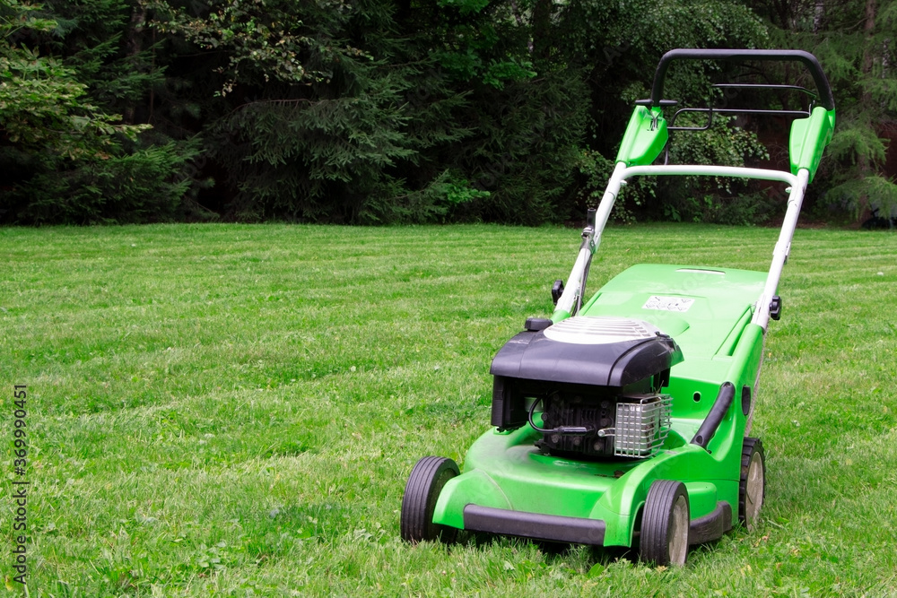 A green lawnmower in the garden. A lawn mower on the green grass. Gardening A green lawnmower in the garden. A lawn mower on the green grass. Gardening