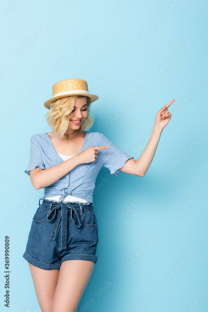 woman in straw hat pointing with fingers and looking away on blue woman in straw hat pointing with fingers and looking away on blue