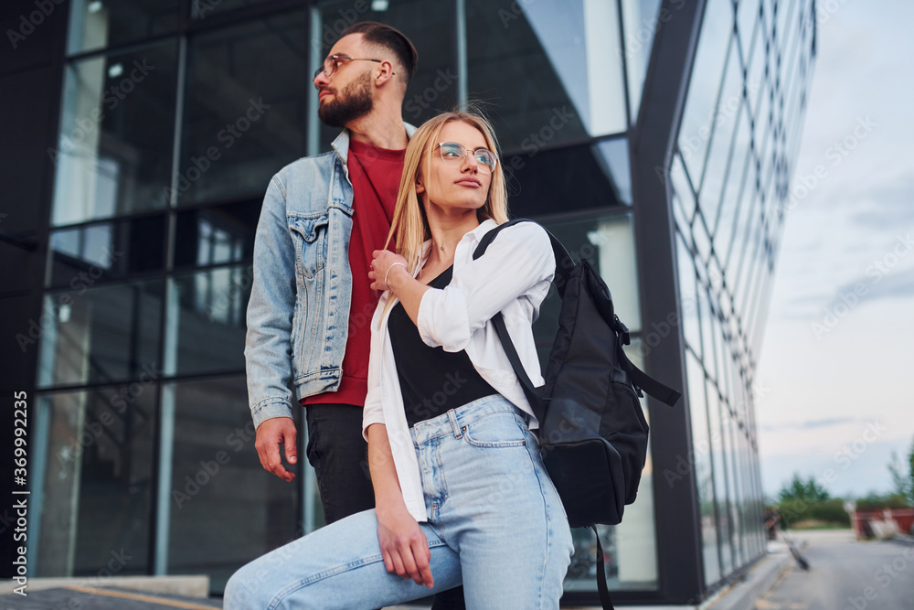 Young stylish man with woman in casual clothes outdoors together near business building. Conception of friendship or relationships