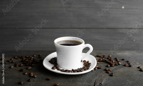 Coffee cup with roasted coffee beans on wooden table background. Mug of black coffe with scattered coffee beans on a wooden table. Fresh coffee beans.