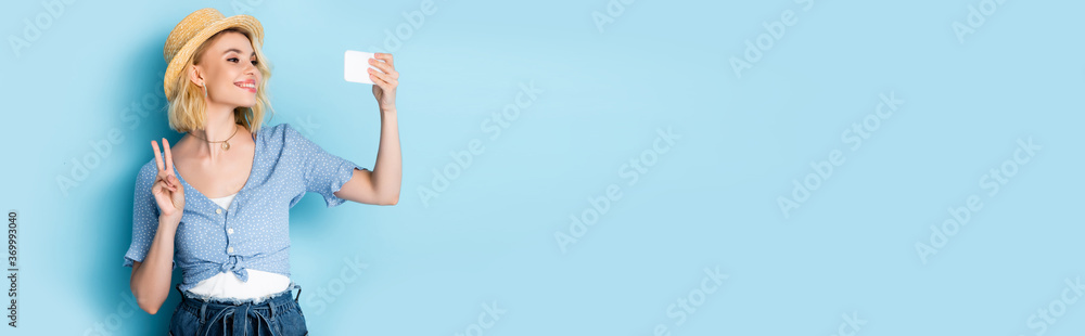 horizontal crop of young woman in straw hat showing peace sign and taking selfie on blue horizontal crop of young woman in straw hat showing peace sign and taking selfie on blue