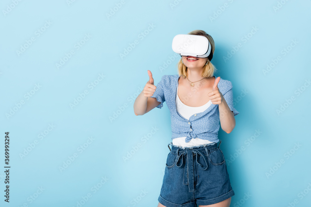 young woman in virtual reality headset showing thumbs up on blue young woman in virtual reality headset showing thumbs up on blue