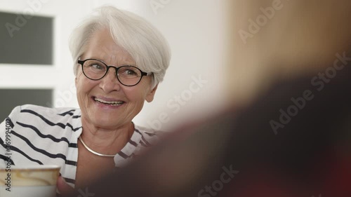 Senior woman with glasses and white hair drinking tea coffee and laughing. Retirement concept. High quality 4k footage photo