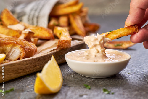 Hand hold a french fries and dips it in sauce tartar