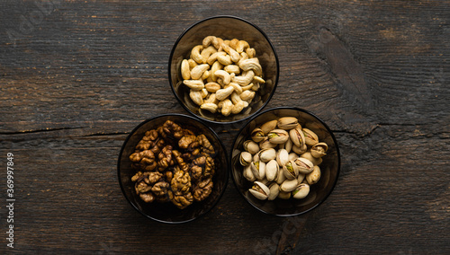 Walnut, pistachio and cashew in a small plates which standing on a black table. Nuts is a healthy vegetarian protein and nutritious food.