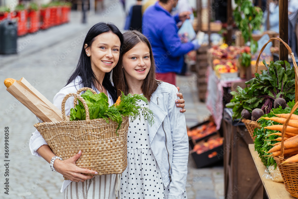Adorable beautiful mother with her teenager daughter buying fresh vegetables at the farmer's market