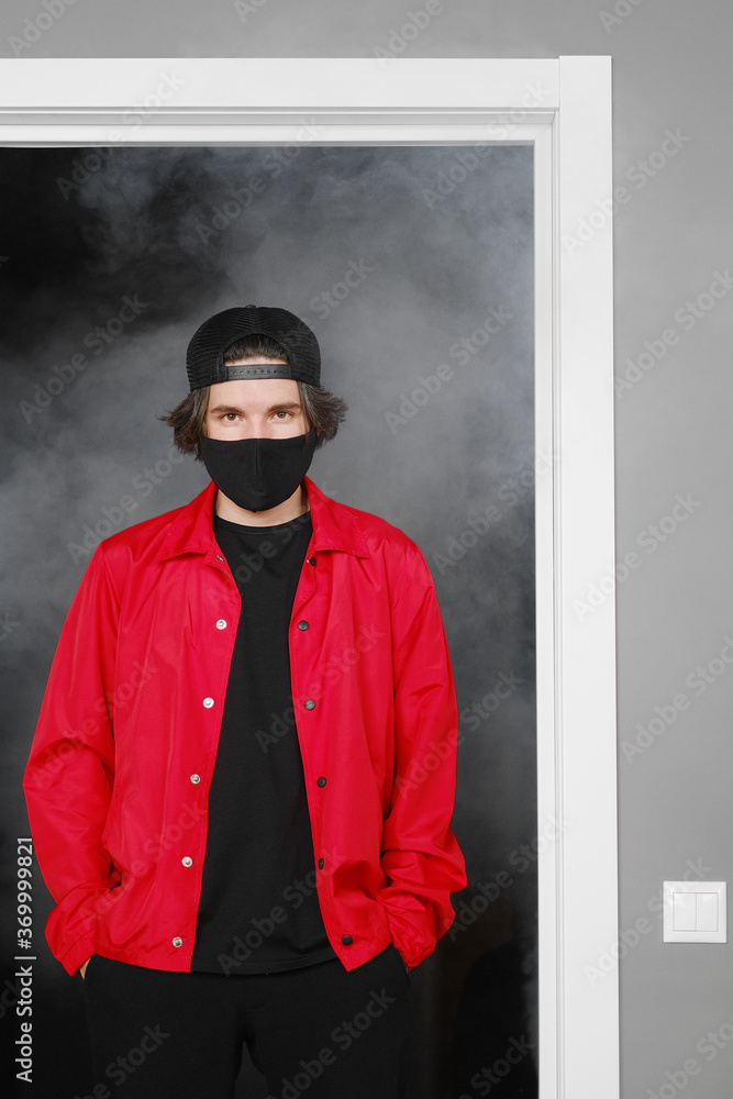 Portrait of a young man of 25-30 years old in a black protective mask, cap and red jacket. Portrait of a young man of 25-30 years old in a black protective mask, cap and red jacket.