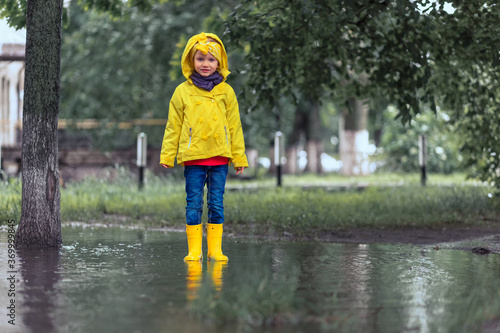 Fototapeta Naklejka Na Ścianę i Meble -  Do not be sad. child girl in yellow raincoat and rubber boots in puddle on a parking, autumn walk. Childhood happiness concept