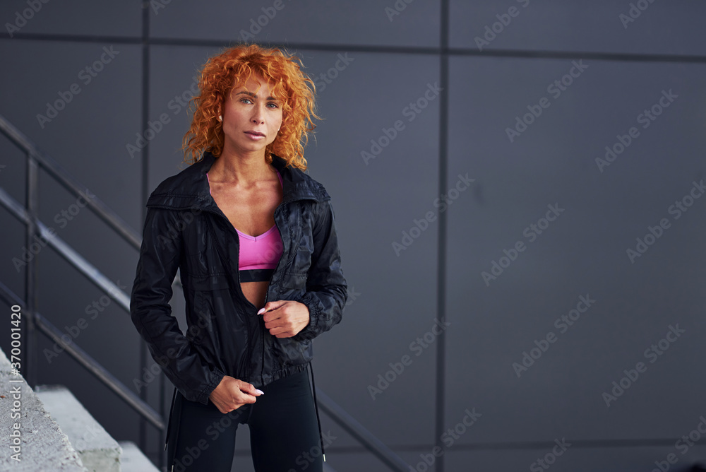 Fototapeta premium Young european redhead woman in sportive clothes standing outdoors