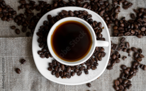 Coffee cup with roasted coffee beans on linen background. Mug of black coffe with scattered coffee beans. Fresh coffee beans. © Volodymyr