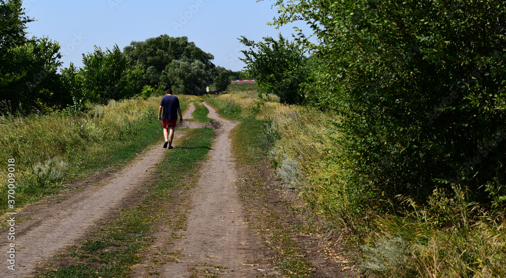 a man walks along the road along the fields