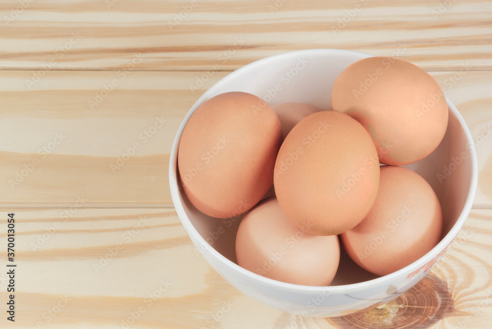 Raw chicken eggs in a white bowl on wooden table, horizontal view. Raw chicken eggs in a white bowl on wooden table, horizontal view.