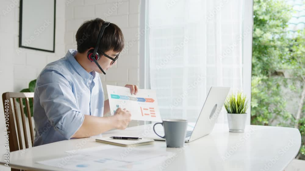 Young Asia businessman using laptop talk to colleagues about plan in video call while smart working from home at living room. Self-isolation, social distancing, quarantine for corona virus prevention.