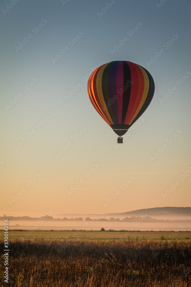 Fototapeta premium Hot Air Balloon floats over fog filled farm field and rolling hills at sunrise