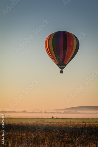 Hot Air Balloon floats over fog filled farm field and rolling hills at sunrise