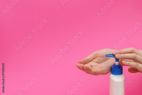 The process of using liquid soap in female hands on pink background.