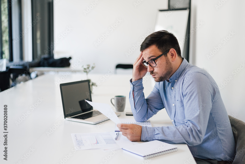 Portrait of stressed out and worried troublesome overworked businessman entrepreneur looking documents report in modern bright office working under pressure and tight deadline empty computer screen Portrait of stressed out and worried troublesome overworked businessman entrepreneur looking documents report in modern bright office working under pressure and tight deadline empty computer screen