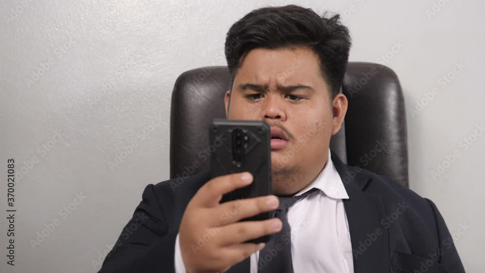 A funny Asian fat businessman wearing a suit look like the head of corporate executive or business manager saw something in his mobile phone that shocked him. A funny Asian fat businessman wearing a suit look like the head of corporate executive or business manager saw something in his mobile phone that shocked him.