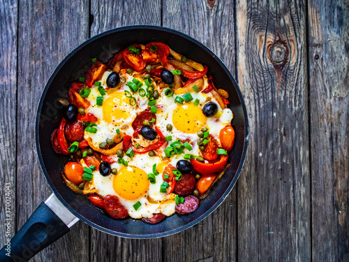Shakshuka - fried eggs with sausages and vegetables in frying pan