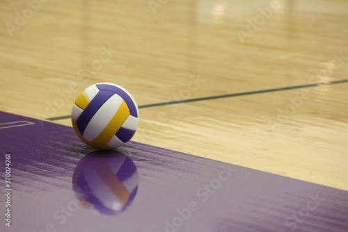 Purple and yellow volleyball on wooden gym floor with purple and black lines