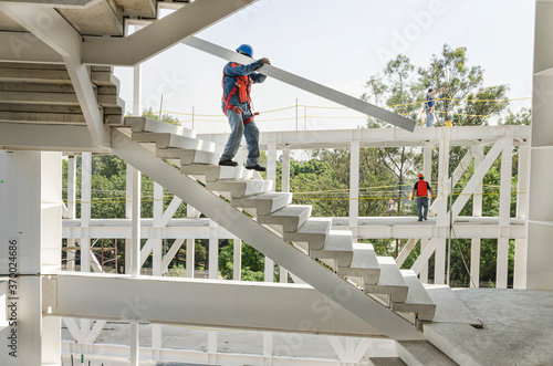 Manual worker carrying down a metallic joist Moving down while balancing a heavy girder through a staircase