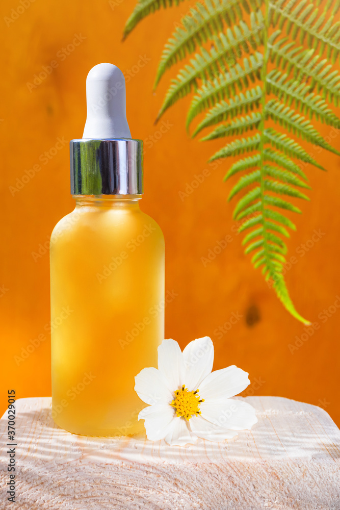 A cosmetic bottle with natural essential oil on a yellow wooden background. Nearby - fern leaves. The concept of organic essences, natural beauty and health products. Modern apothecary. A cosmetic bottle with natural essential oil on a yellow wooden background. Nearby - fern leaves. The concept of organic essences, natural beauty and health products. Modern apothecary.