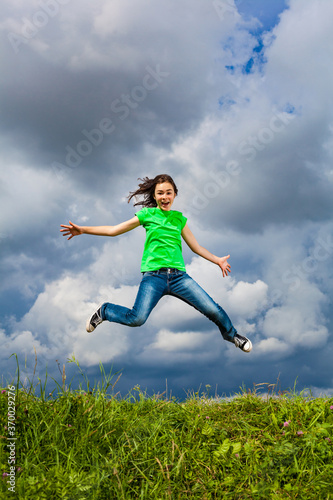 Girl jumping, running against cloudy sky 