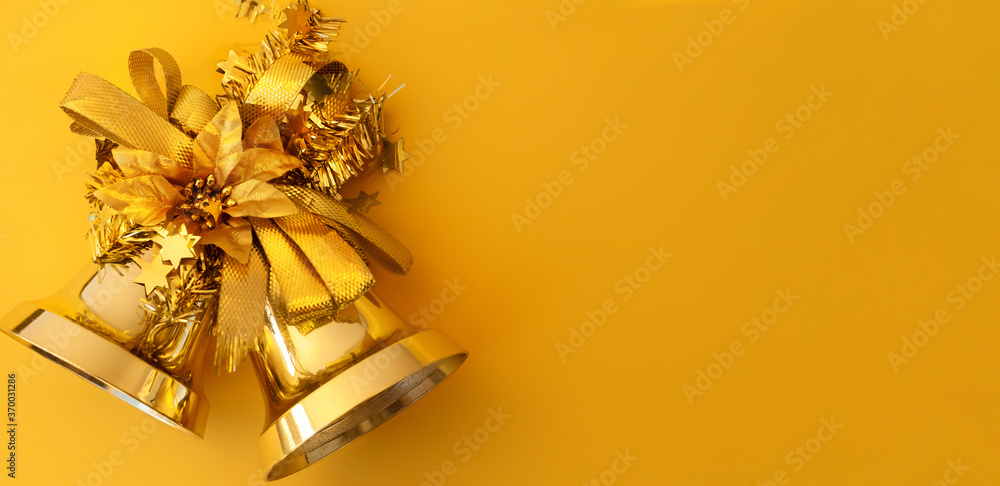 Φωτογραφία Gold Christmas bells with ribbons and poinsettia on a yellow background with copy space