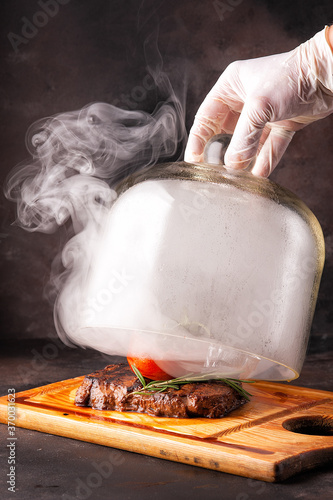 The chef opens a glass cover of meat and rosemary.