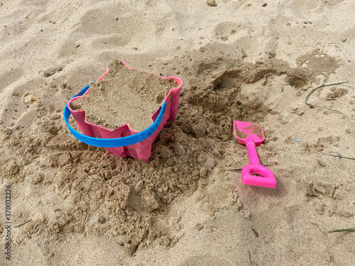 Pink Bucket and spade building a sand castle on the sand's hills on Great Yarmouth beach in a cold summer day, traditional UK, English East Coast, sky with clouds no people, large stretch of sand, UK  photo