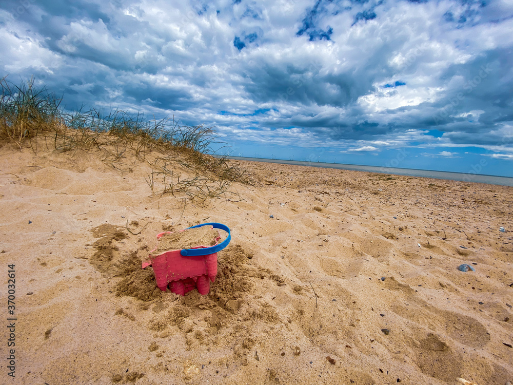 Pink Bucket and spade building a sand castle on the sand's hills on Great Yarmouth beach in a cold summer day, traditional UK, English East Coast, sky with clouds no people, large stretch of sand, UK Pink Bucket and spade building a sand castle on the sand's hills on Great Yarmouth beach in a cold summer day, traditional UK, English East Coast, sky with clouds no people, large stretch of sand, UK