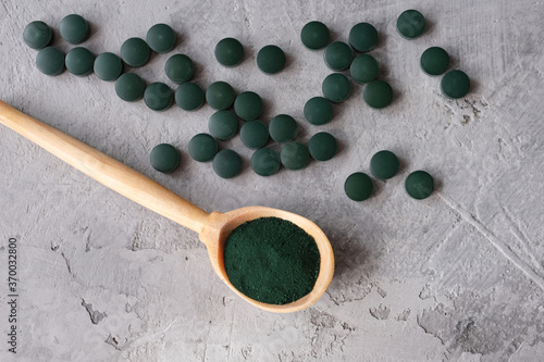 Green chlorella powder in wooden spoon and green chlorella tablets on gray concrete background. Chlorella is a single-celled green algae, it is used to make nutritional supplements and medicine. Top v