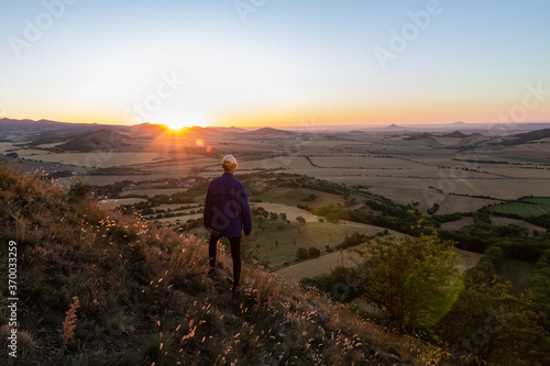 Young man with backpack walking down from hill and looking to Czech ore mountain valley at sunrise landscape