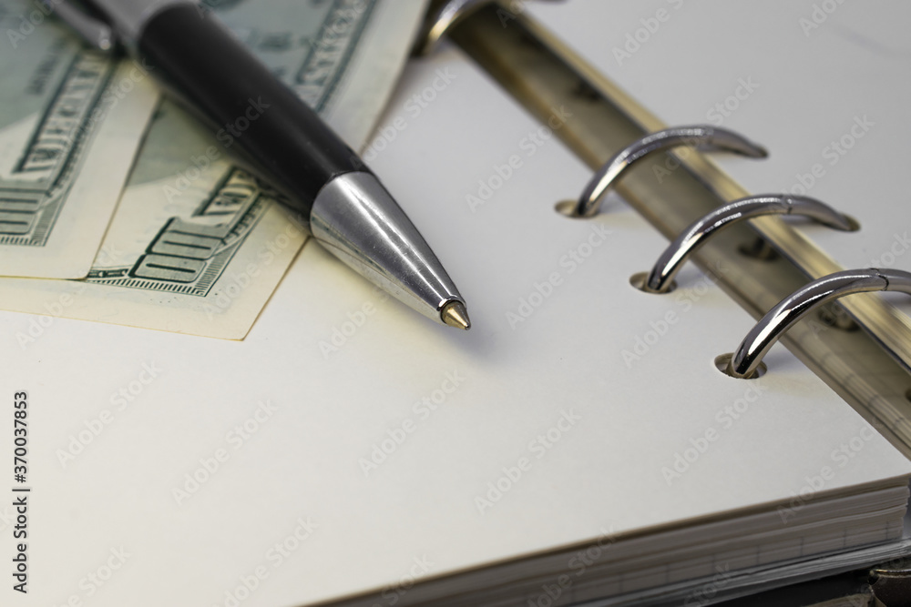 the pen is on top of an open Notepad with dollars the pen is on top of an open Notepad with dollars