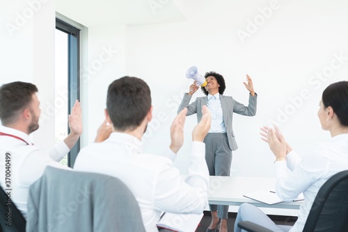 Colleagues applauding woman announcing good news on megaphone