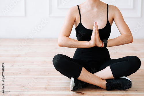 Close-up of Young woman sitting cross-legged on the floor and holding folded palms in front of her during meditation