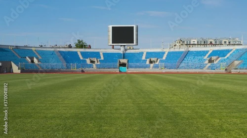 Empty sports stadium with nobody from football field. Travelling in through the grass to big scoreboard.